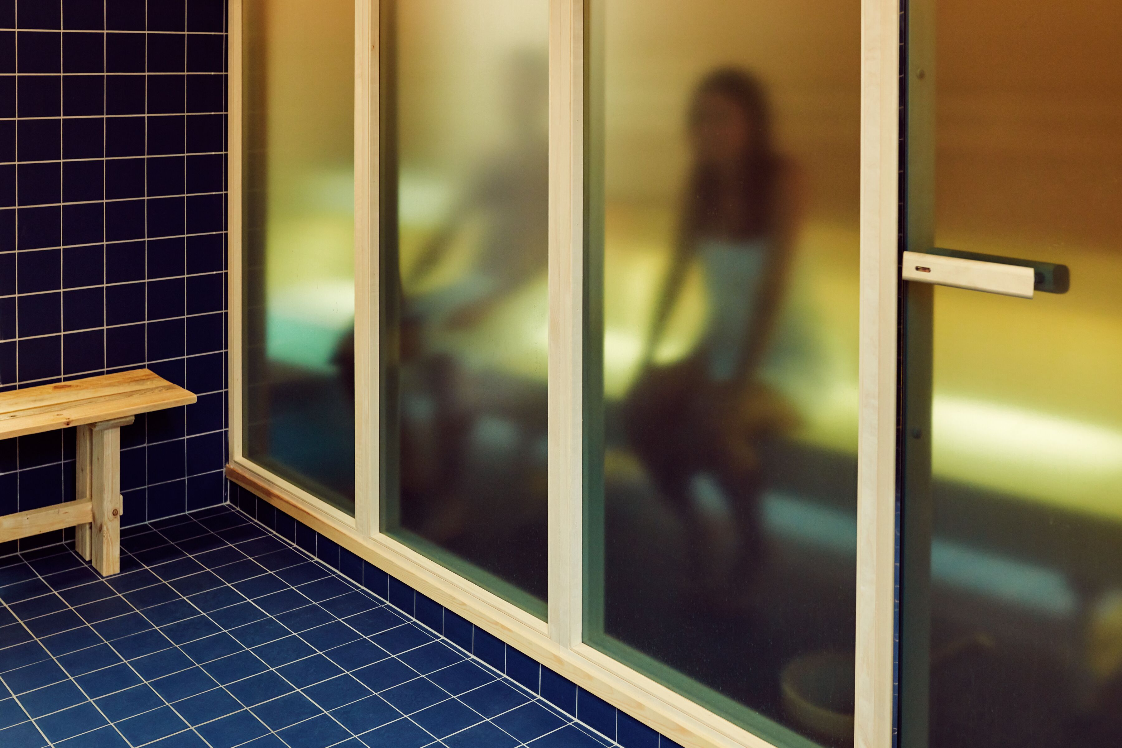 A room with a wooden bench, tiled floor, and large frosted glass doors.