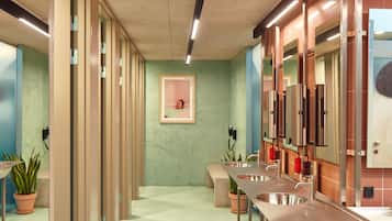 Un baño con varios lavamanos, un banco y plantas en macetas.