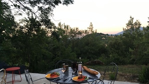 An outdoor dining area with a round table, metal chairs, and a bottle of wine. - Charming stone house in the countryside (Céret)