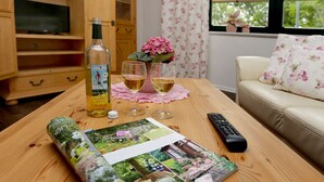 Ein Holztisch mit einer Flasche, zwei Weingläsern, einer Fernbedienung und einer Zeitschrift.