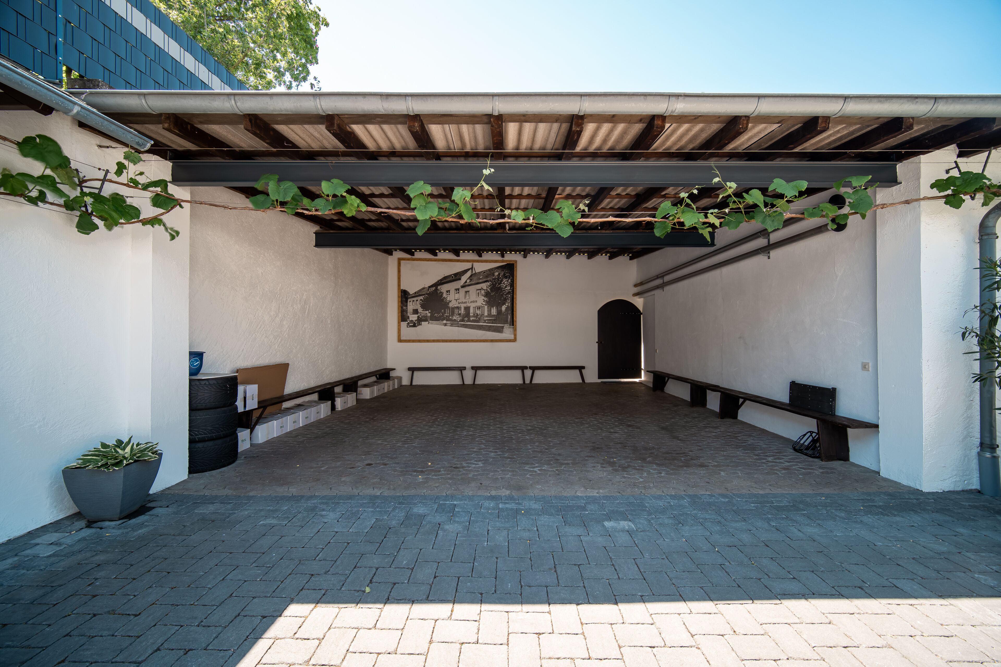 An outdoor covered patio area with a brick floor, benches, and a potted plant.