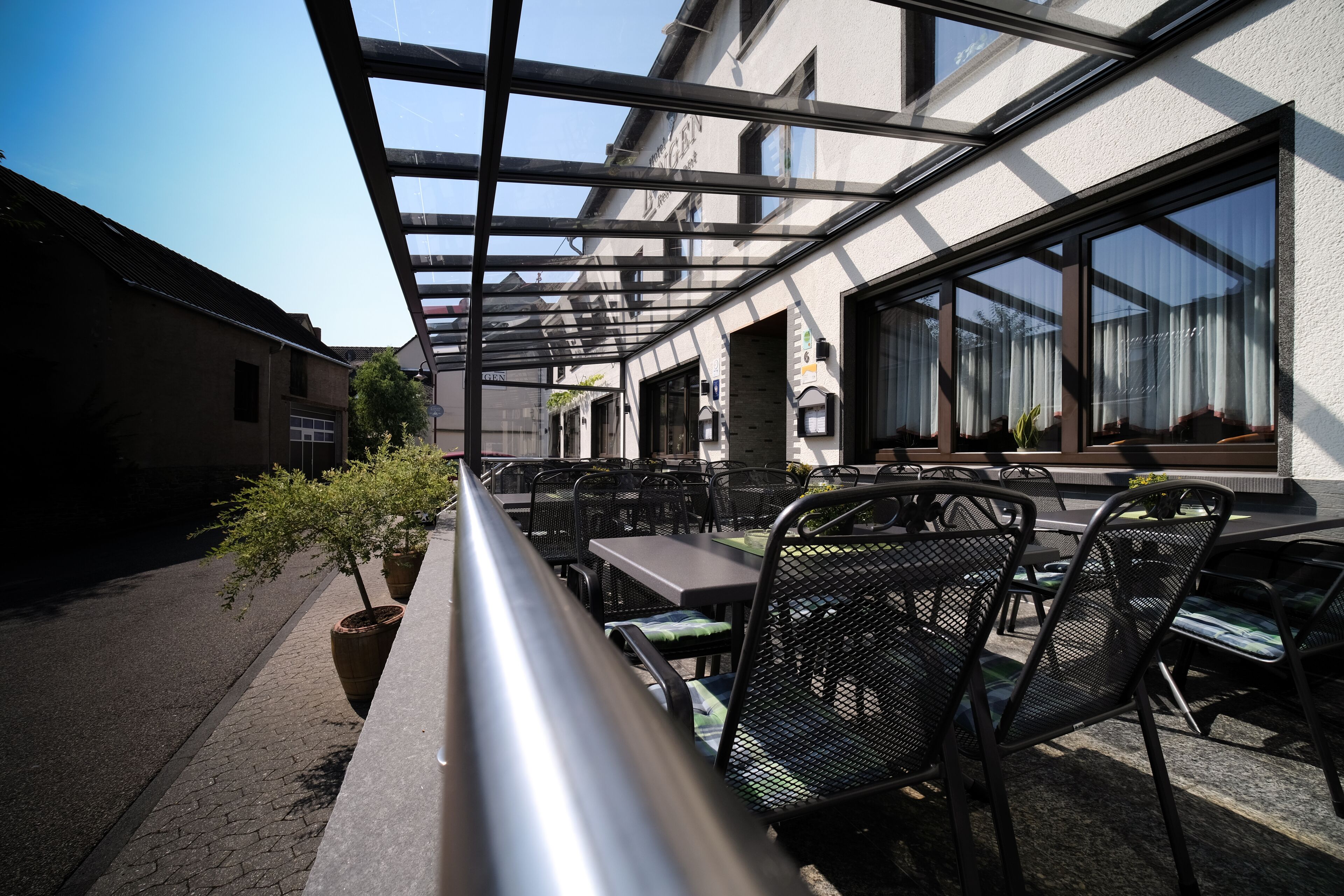 Une terrasse extérieure avec des tables et des chaises, une rambarde en verre et des plantes en pot.