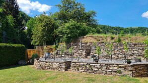 A stone retaining wall with plants and a barrel. - Hotel Langen (Loef)