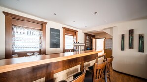 A bar area with wooden counter and stools, a chalkboard menu, and shelves with glasses and bottles. - Hotel Langen (Loef)
