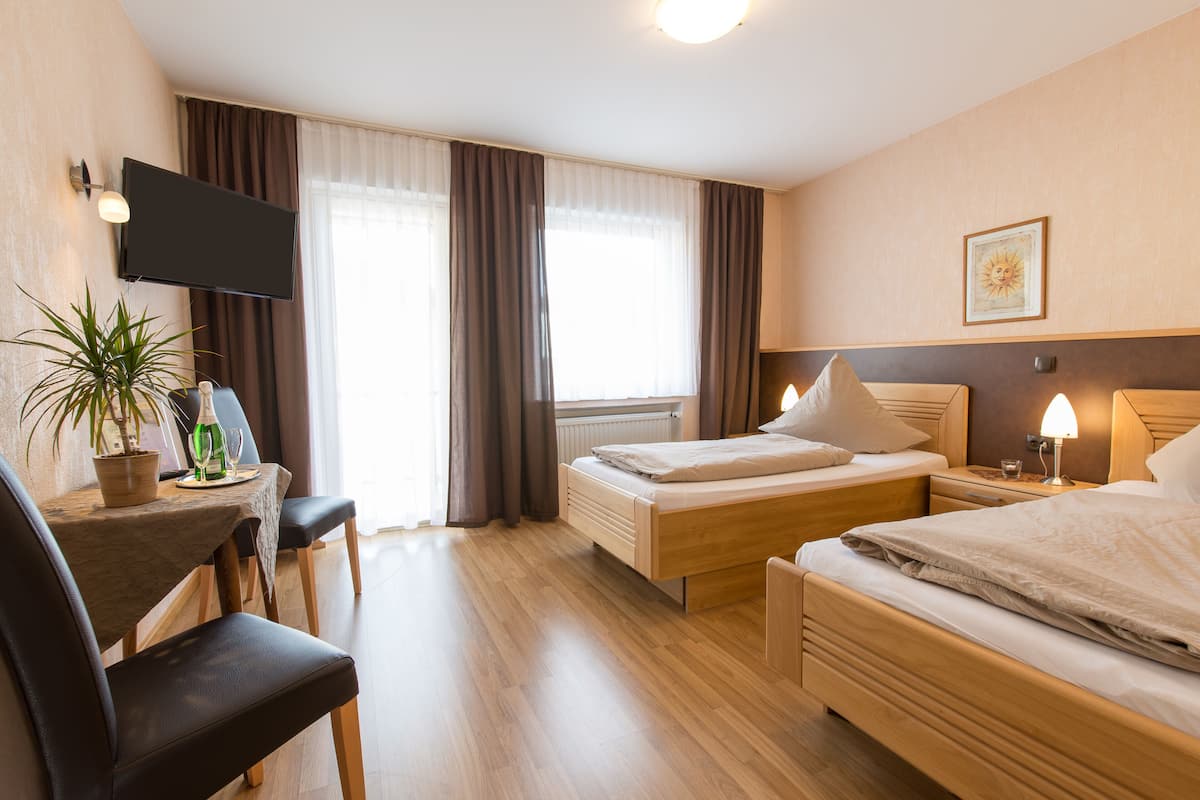 A hotel room with two beds, a desk with a chair, a flat-screen TV, a potted plant, and a window with curtains.