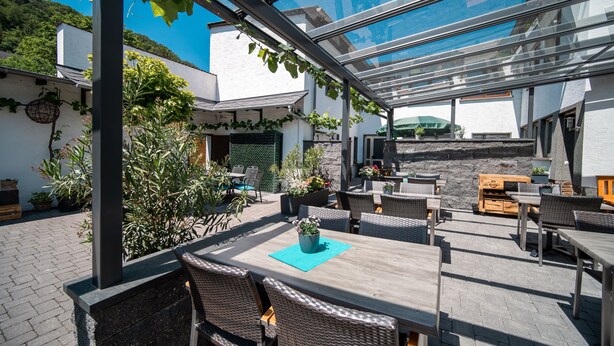 An outdoor patio area with tables and chairs, a glass enclosure, and potted plants. - Hotel Langen (Loef)