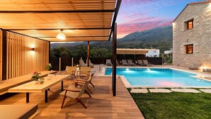 Zona de piscina amb terrassa de fusta, gandules, una taula de menjador i vista a les muntanyes.