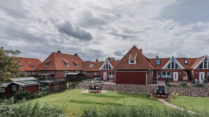 Een rij rode bakstenen huizen met puntdaken en een gazon met tuinmeubilair.
