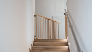 Een houten trap met een leuning, leidend naar een deur met een lichtschakelaar en stopcontact op de muur.
