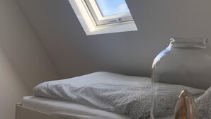Een kamer met dakraam, een bed met gestreept beddengoed en een glazen vaas op een tafel.