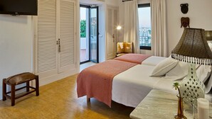 Ein Schlafzimmer mit Bett, Nachttisch, Fernseher, einem Fenster mit Vorhängen und Blick auf die Stadt.