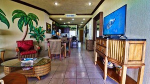 A spacious living area with wicker furniture, a television, and a kitchen in the background.