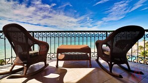 A balcony with wicker furniture, a small table, and a view of the ocean.