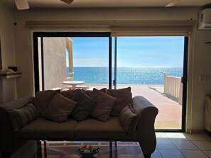 Ein Wohnzimmer mit einer Couch, einem Glastisch und Meerblick durch große Schiebetüren.