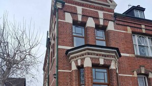Un bâtiment en briques rouges, avec une entrée située à l’angle, un petit porche et un escalier menant à l’entrée.