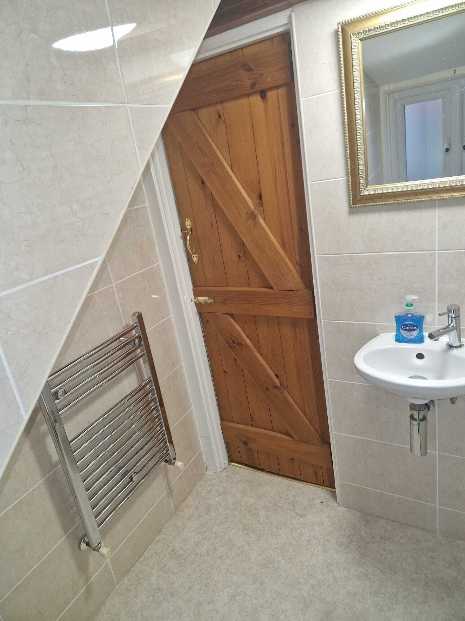 A bathroom with a wooden door, a white sink, and a mirror.