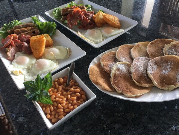 Un desayuno abundante con huevos, tocino, frijoles y panqueques sobre una mesa de granito.