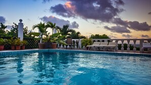 A pool with lounge chairs and potted plants, surrounded by a fence and palm trees. - Beautiful supersize villa perfect for larger families and groups. Sleeps 22 (Cap Estate)