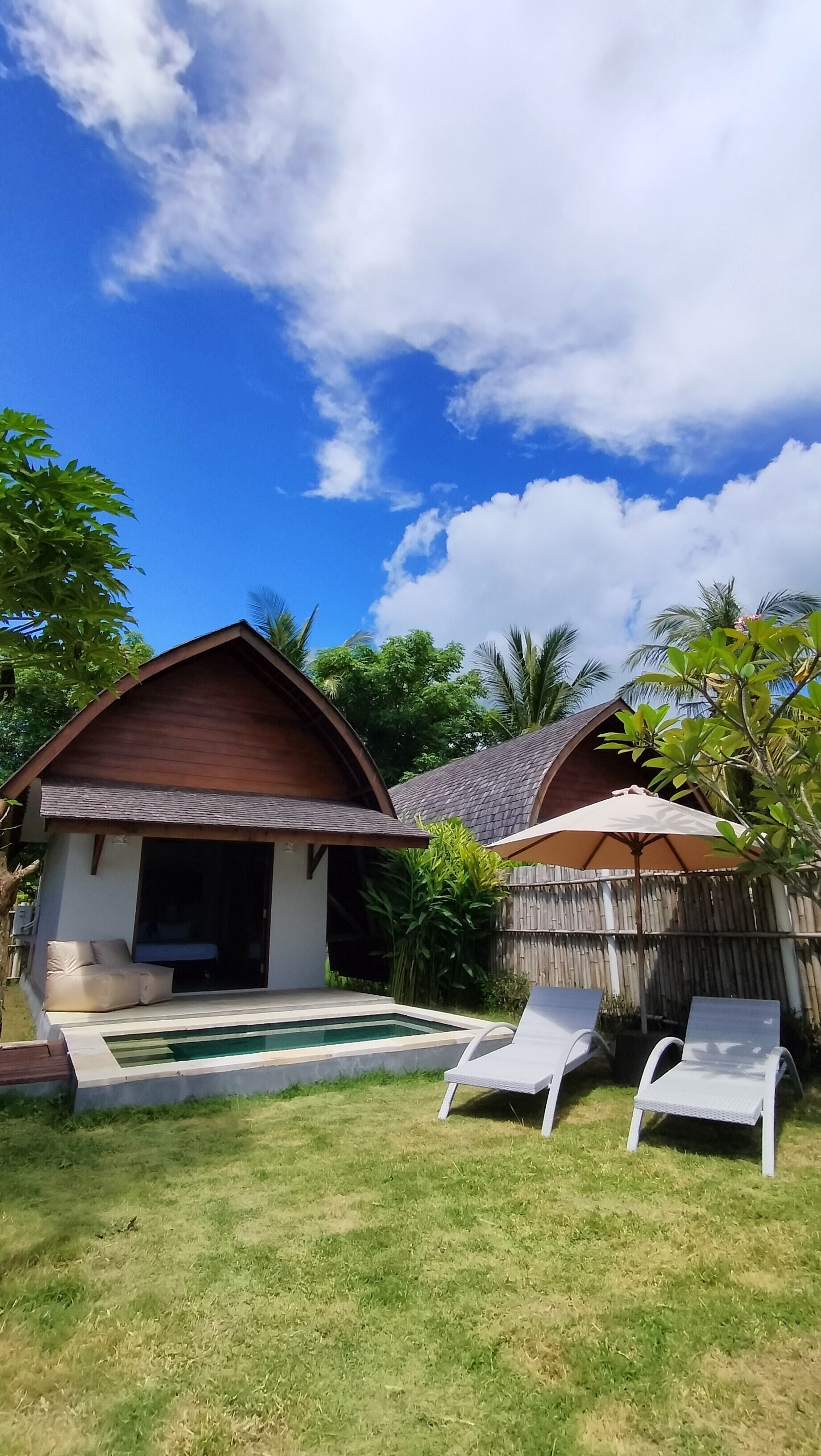 A modern house with a swimming pool, two lounge chairs, and a covered patio area.
