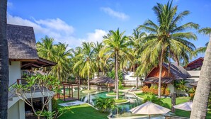 Ein Resort mit Schwimmbad, Liegestühlen, Palmen und einem Gebäude mit Strohdach.