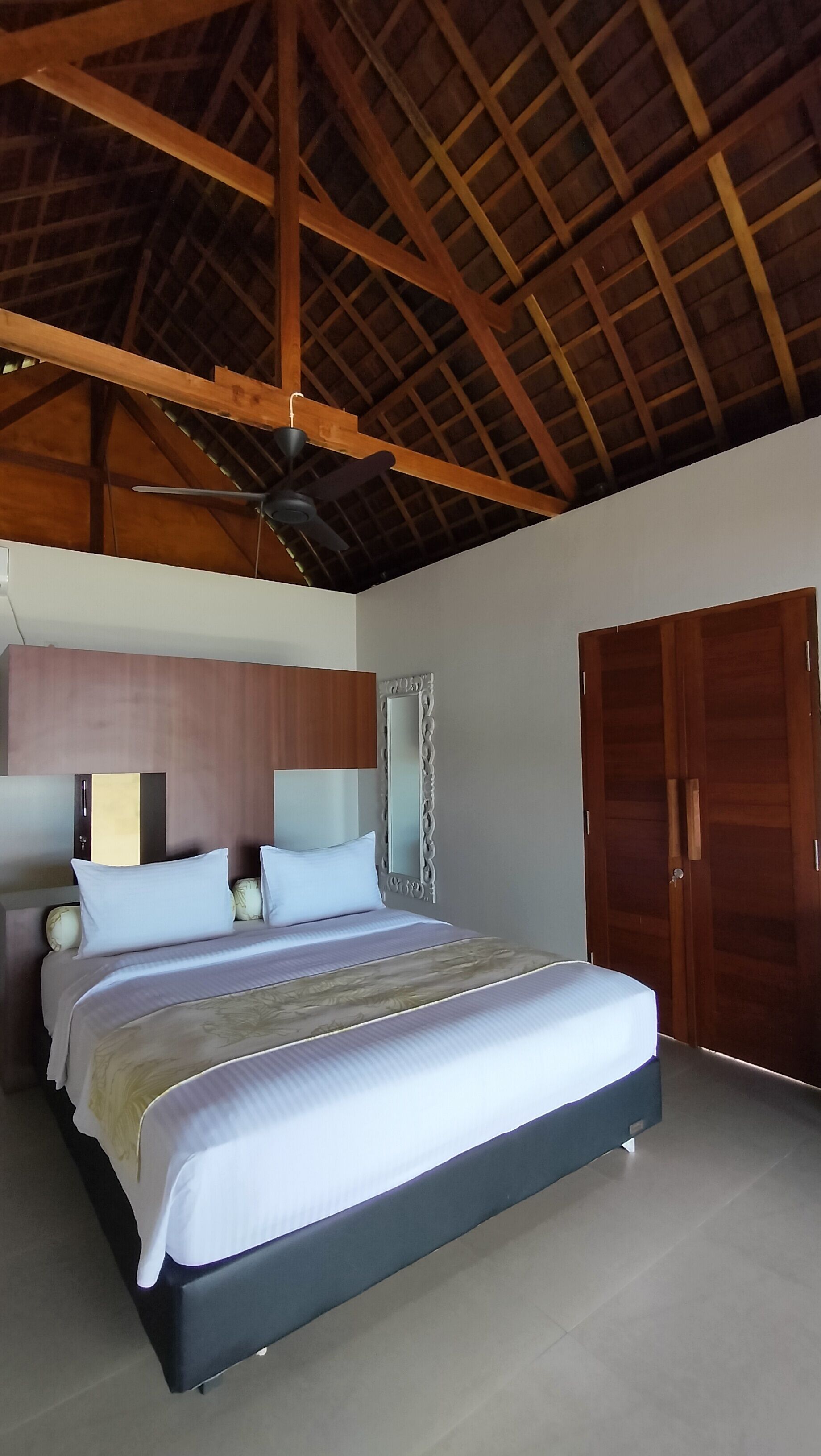 Un dormitorio con una cama grande, vigas de madera en el techo, un ventilador de techo y un armario.