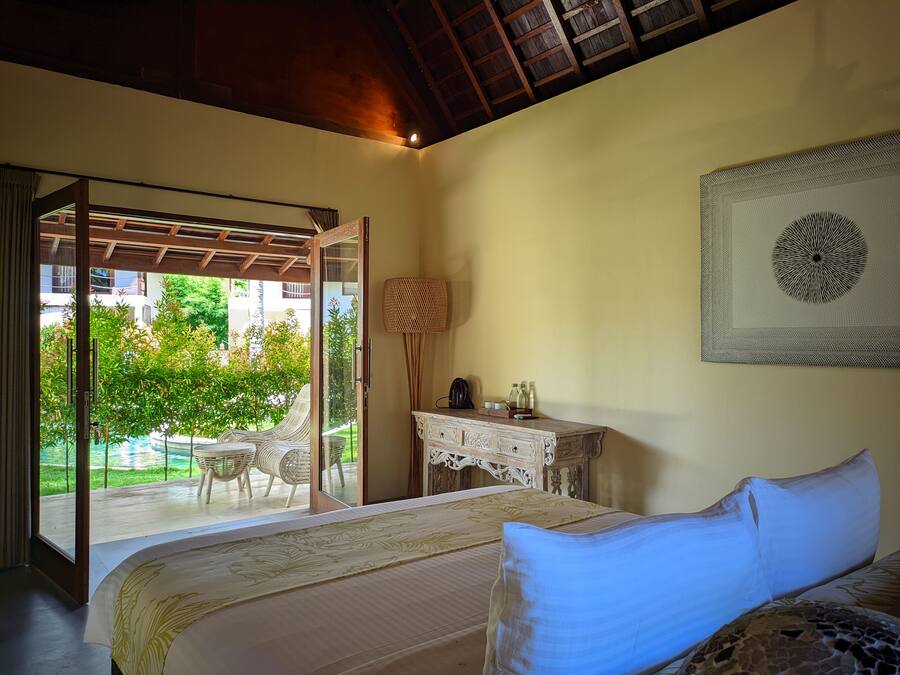Un dormitorio con cama, escritorio y vista a un jardín a través de un ventanal.
