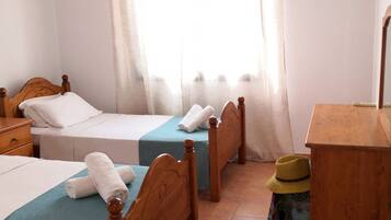 Camera d'albergo con due letti singoli, una scrivania in legno, uno sgabello e un'ampia finestra con tende.
