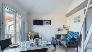 Zona pranzo con tavolo imbandito per quattro persone, televisione a parete e poltrona blu con motivi floreali.