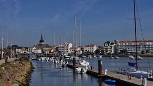A marina with boats docked, a stone wall, and buildings in the background. - Between town centre and beach, house for 6 (Saint-Gilles-Croix-de-Vie)