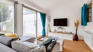 A modern living room with a sofa, a coffee table, a flat-screen TV, and a sliding glass door leading to an outdoor area. - Between town centre and beach, house for 6 (Saint-Gilles-Croix-de-Vie)