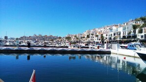 A marina with boats docked, a clear blue sky, and buildings with balconies in the background.
