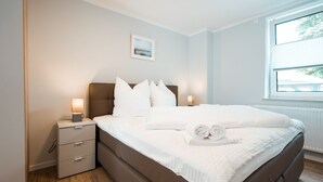 Une chambre avec un grand lit, des tables de chevet, une fenêtre et un tableau encadré au mur.