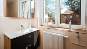 Une salle de bain moderne avec un lavabo blanc, des meubles noirs et une fenêtre donnant sur un bâtiment en briques et des arbres.