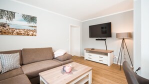 Un salon moderne avec un canapé marron, une table basse en bois, un téléviseur à écran plat et un lampadaire.