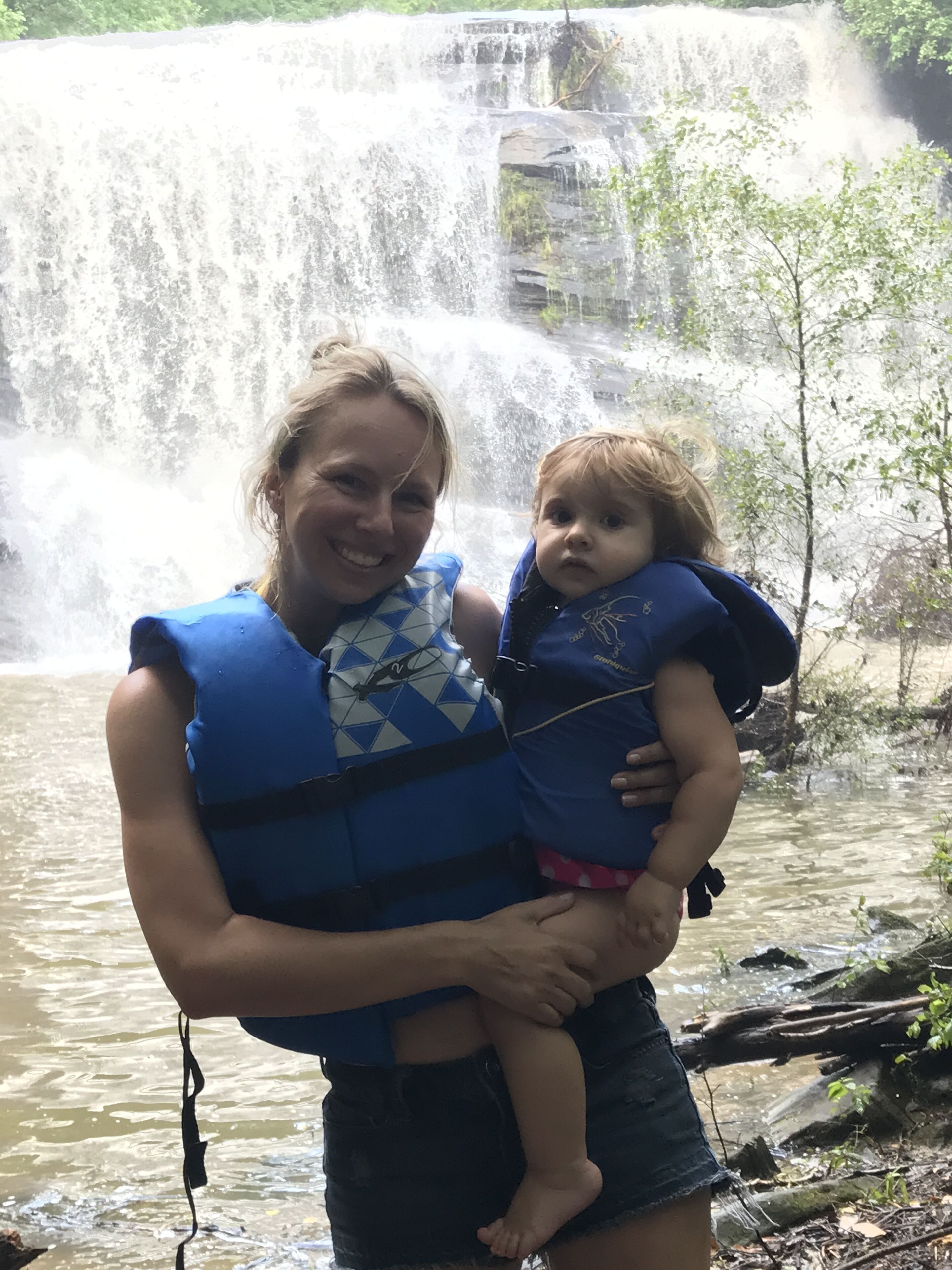 A person holding a child near a waterfall.