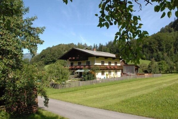 A two-story house with a balcony, surrounded by a well-maintained lawn and trees. - Hinterkellaubauer (Kuchl)