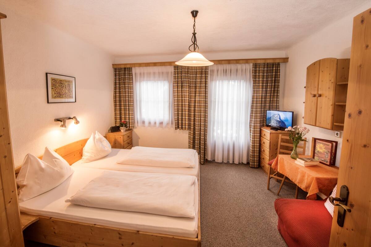 A room with two beds, a desk with a television, and a window with curtains.