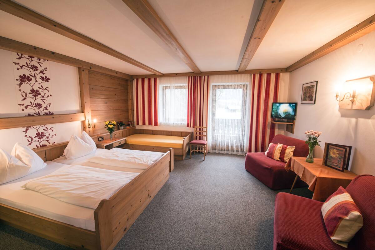 A cozy room with a wooden bed, a red sofa, a small table with a vase, and a TV on a wooden stand.