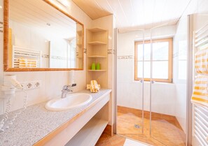 Ein modernes Badezimmer mit einer Granittafel, einem weißen Waschbecken, einem großen Spiegel und einer Duschkabine aus Glas.