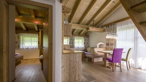 A spacious room with wooden beams, a dining area with a table and chairs, and a cozy seating area with a sofa and cushions. - Feriengut Unterhochstätt (Schwendt)