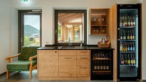 A kitchen with a wooden cabinet, a built-in wine cooler, a chair, and a view through a window.