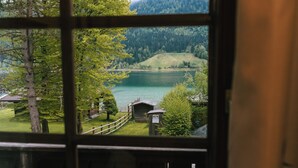 A view through a window of a lake with a wooden deck, a small building, and a forested hillside.