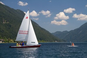 Un velero con pasajeros en un lago rodeado de montañas.