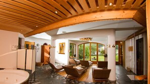 A spacious indoor area with a large wooden ceiling, a hot tub, and several wicker chairs.