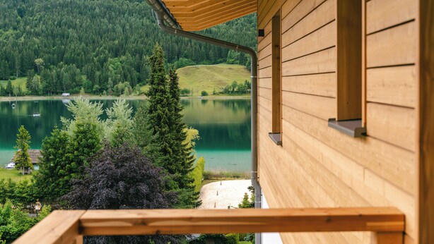 A wooden cabin with a balcony overlooking a lake and forest.