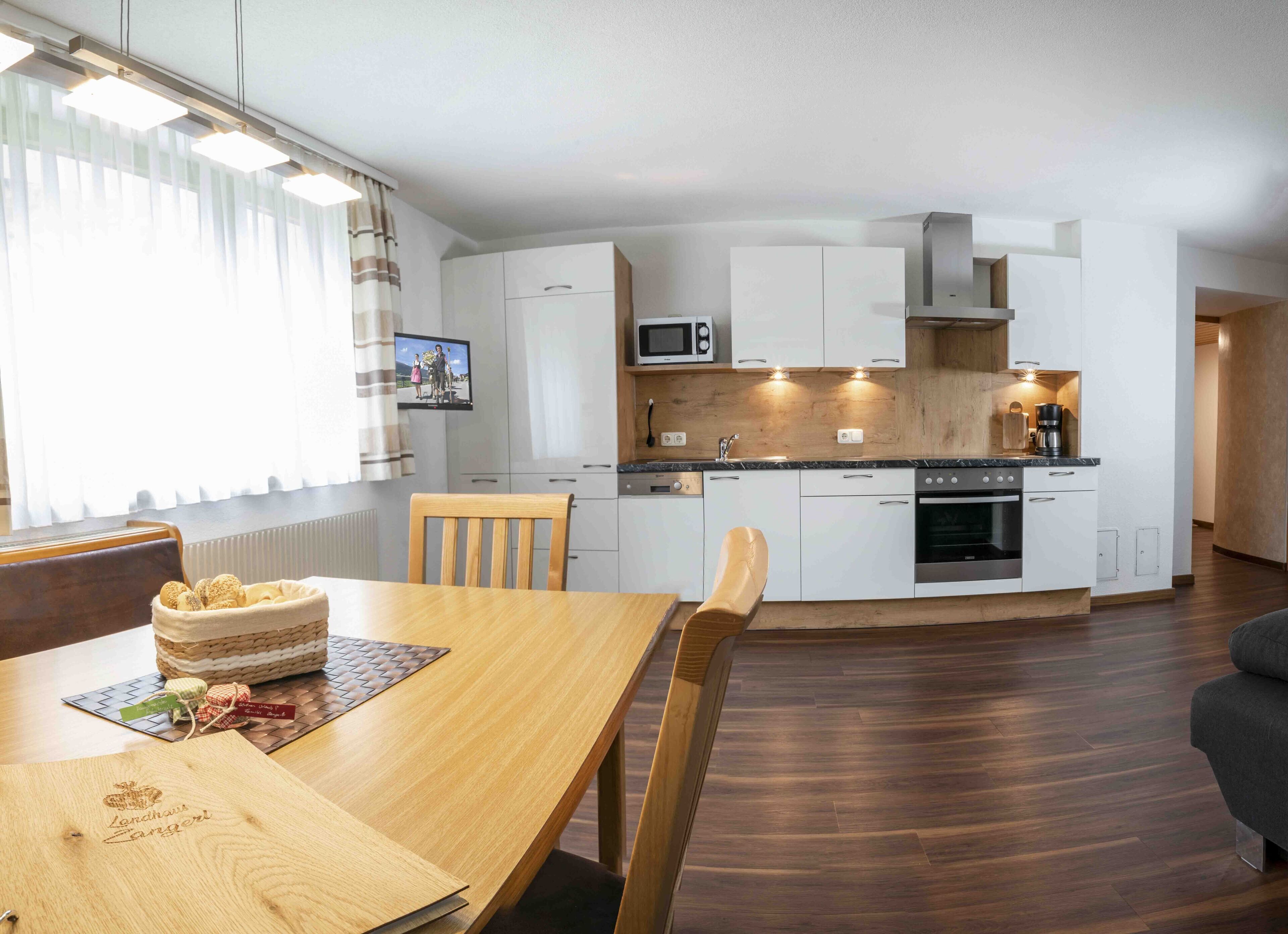A modern kitchen with white cabinets, a microwave, and a built-in oven. There is a dining table with chairs and a basket of bread.