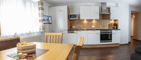 A modern kitchen with white cabinets, a microwave, and a built-in oven. There is a dining table with chairs and a basket of bread.