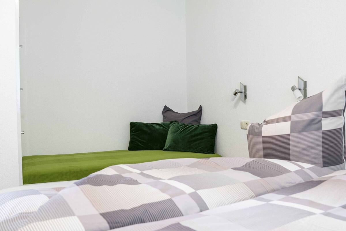 Un dormitorio con cama, almohadas y una lámpara fijada en la pared.