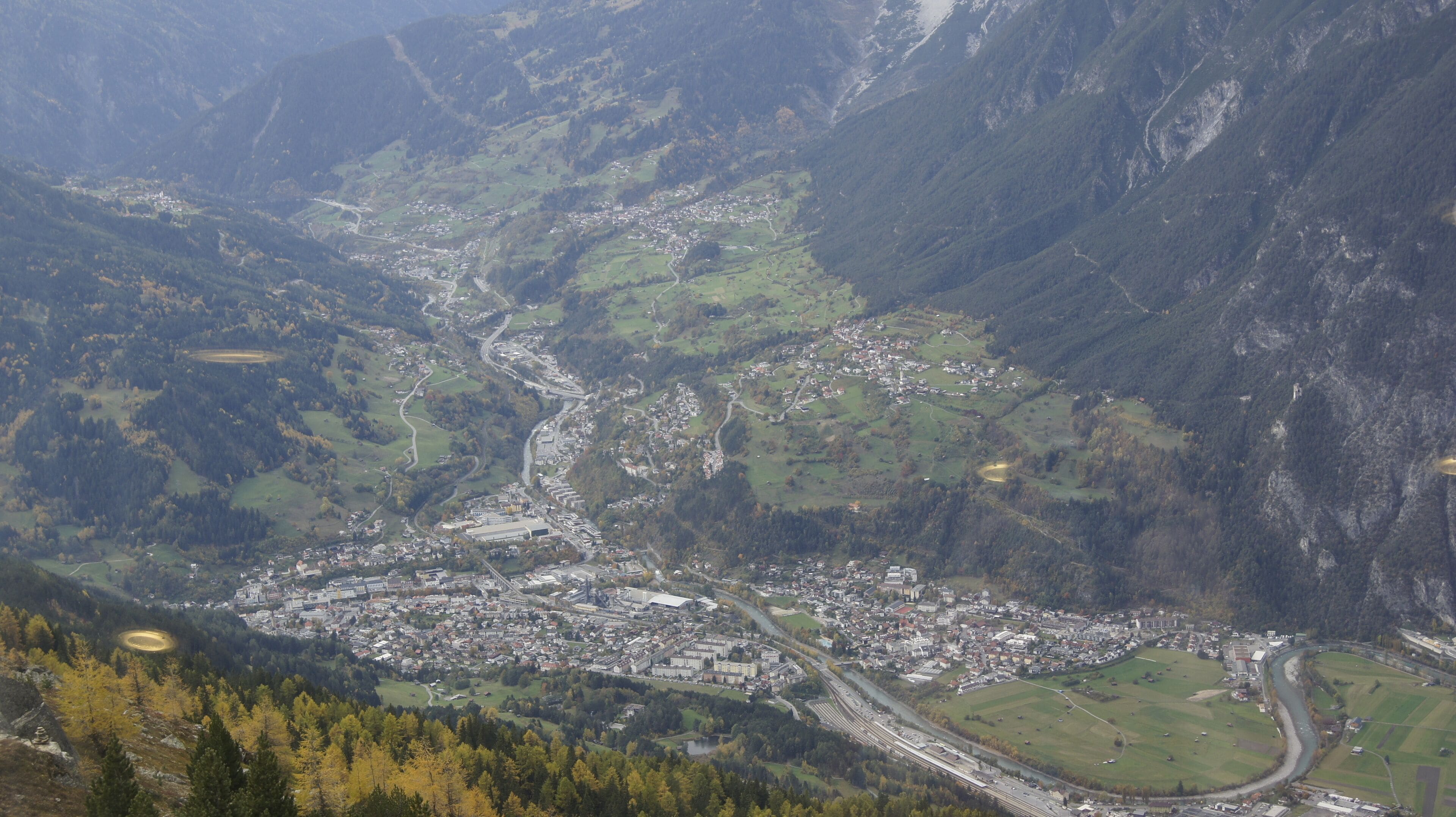 An aerial view of a valley with a town, roads, and surrounding mountains.