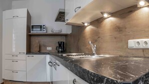 A modern kitchen with white cabinets, a black marble countertop, a built-in microwave, a coffee maker, and a wooden backsplash. - Landhaus Zangerl (Landeck)